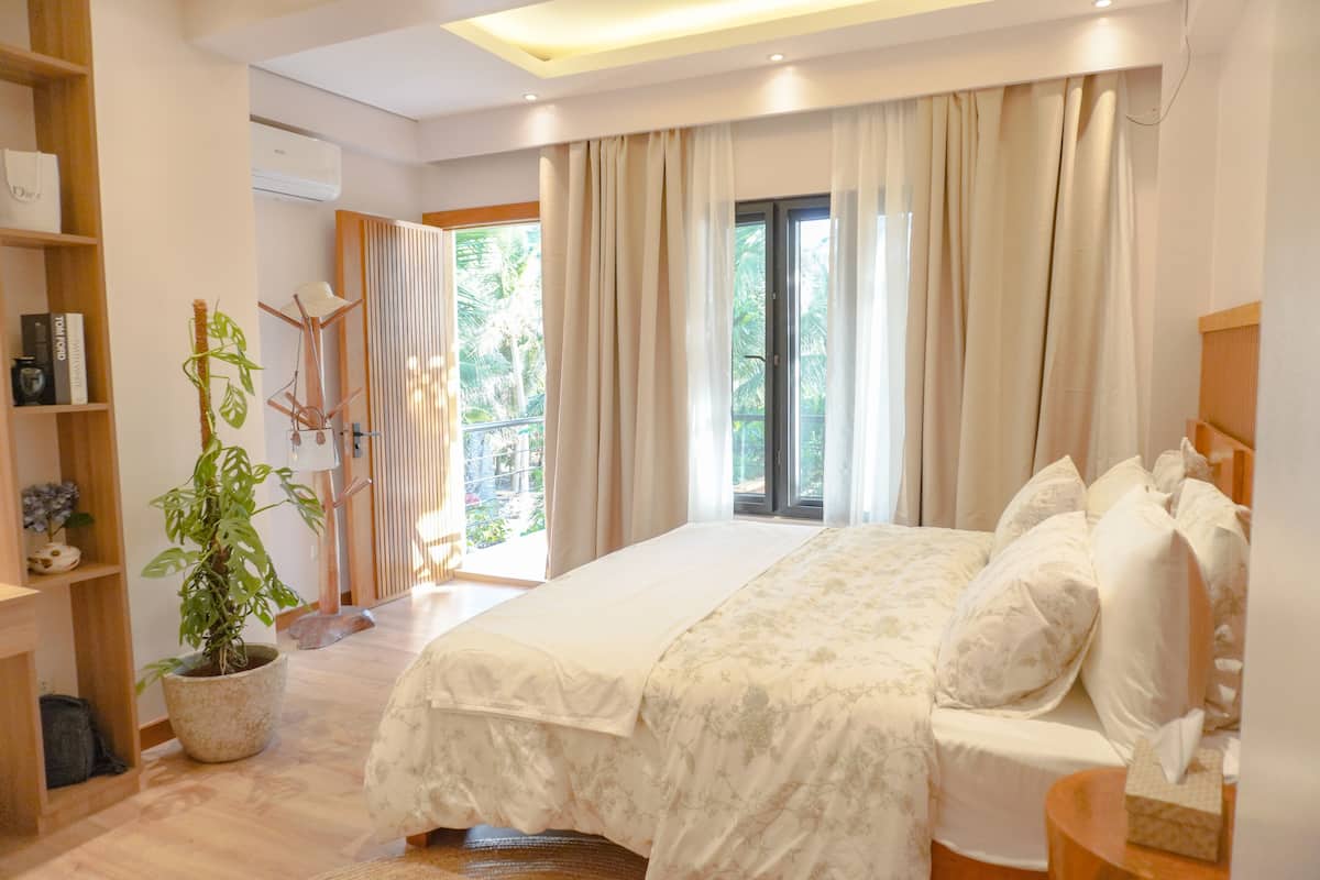 A modern bedroom with a large bed, a potted plant, and a view of the outdoors.