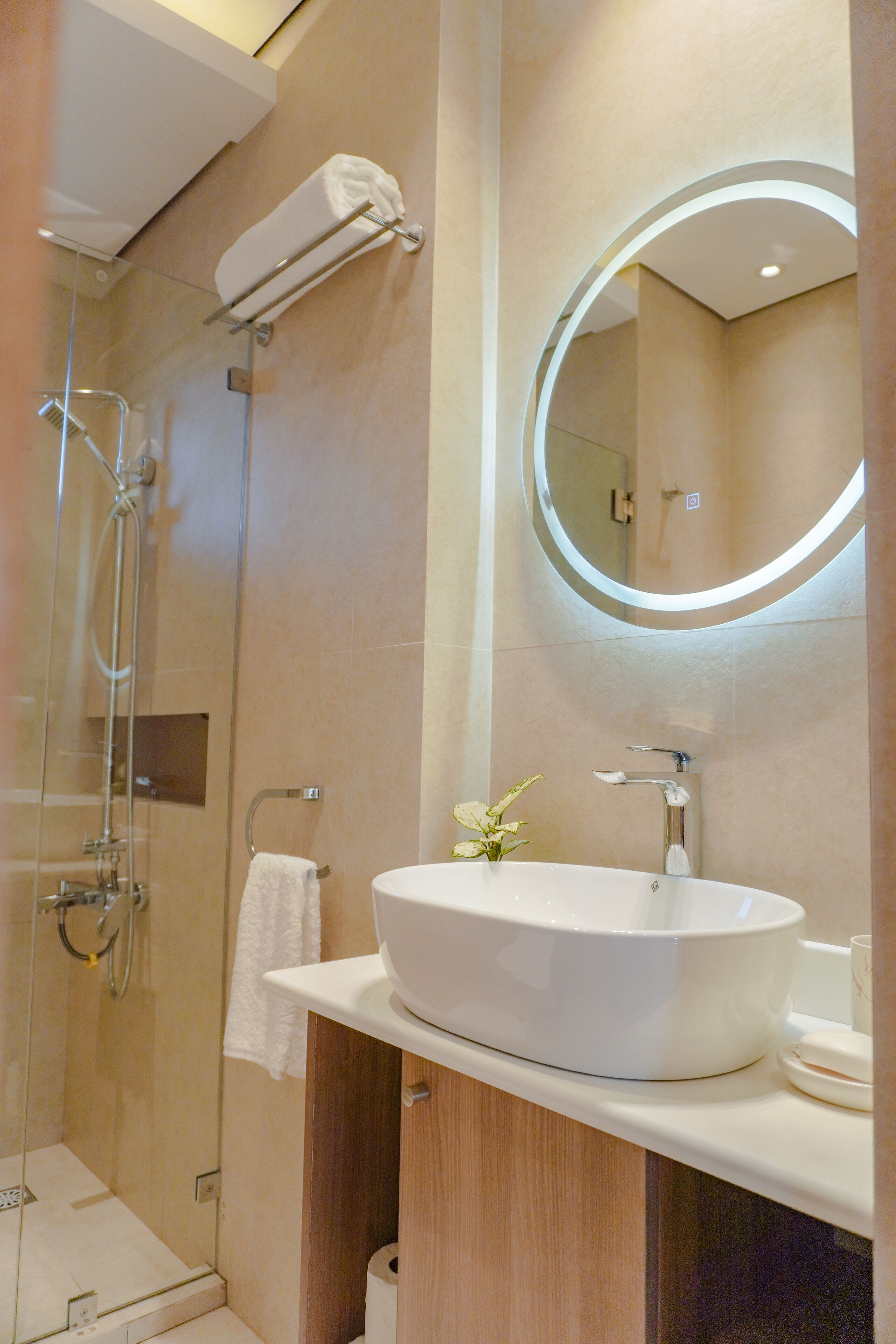 Un baño moderno con ducha de vidrio, un lavamanos blanco y un espejo con luz circular.