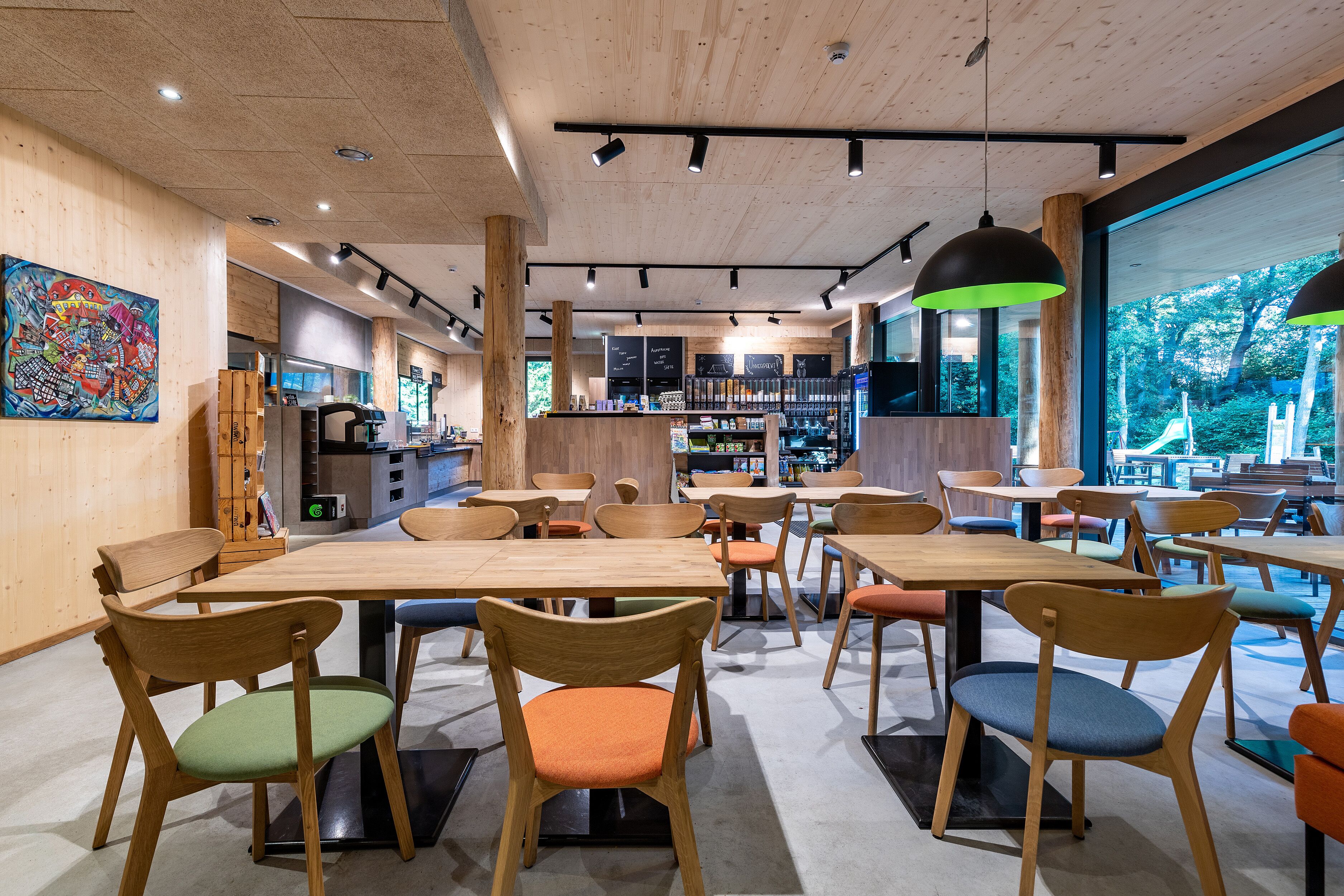 A modern cafe interior with wooden tables and chairs, a bar area, and a view of the outdoors.