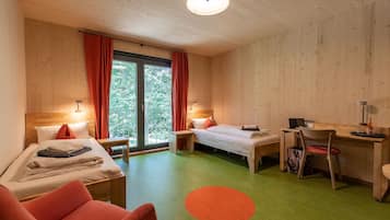 A room with two beds, a desk, and a chair. There is a window with curtains, a lamp, and a red rug.