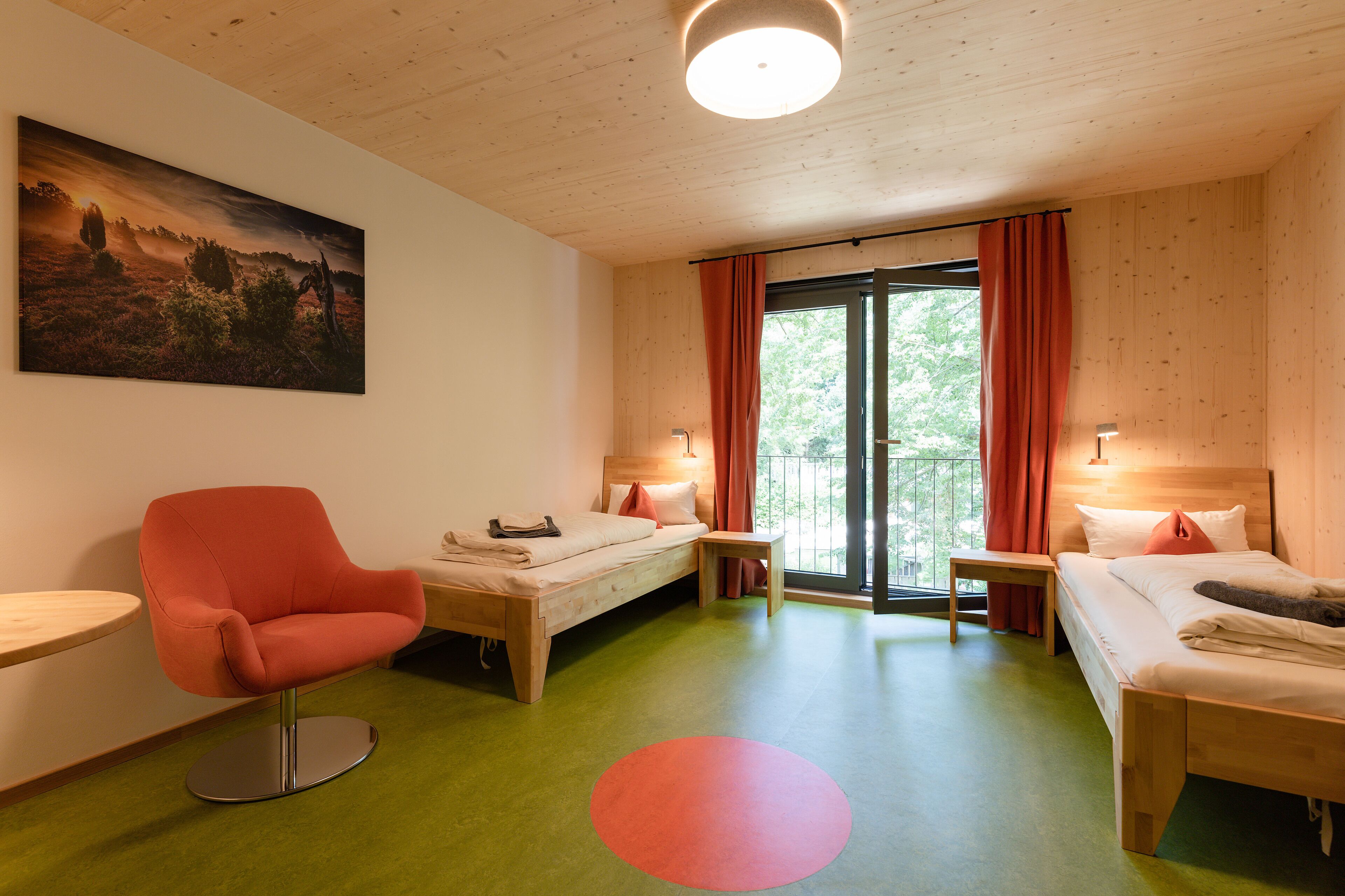 A room with a bed, a chair, a small table, and a painting on the wall.