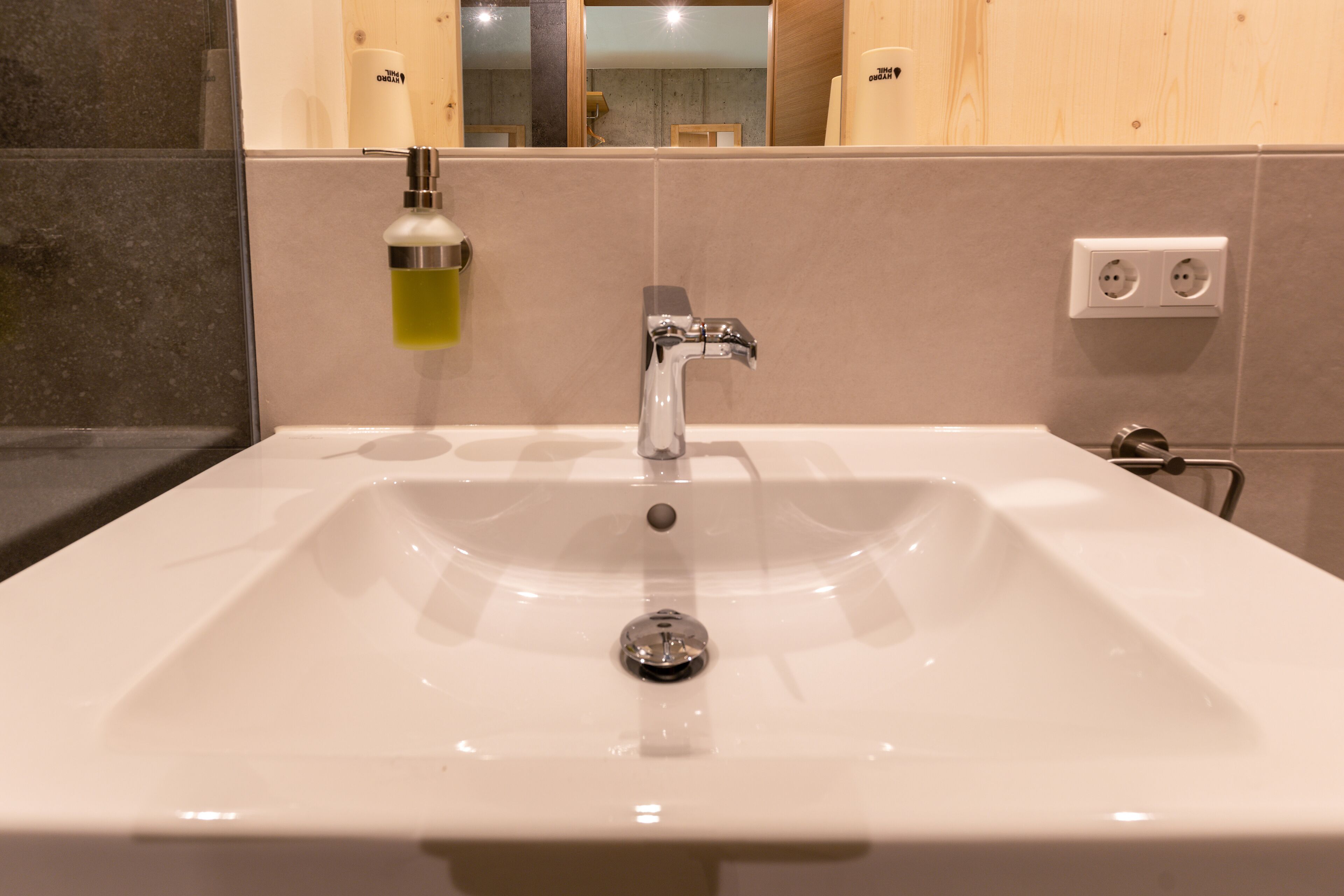 A bathroom with a white sink, a mirror, and a towel dispenser.