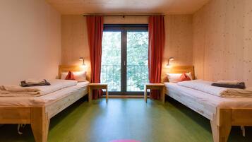 Een kamer met twee houten bedden, een groen tapijt en een balkon met rode gordijnen.