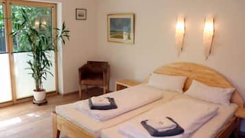 Cama de casal com roupa de cama branca, cabeceira de madeira e duas mesas de cabeceira. Há uma planta em vaso e um quadro na parede.