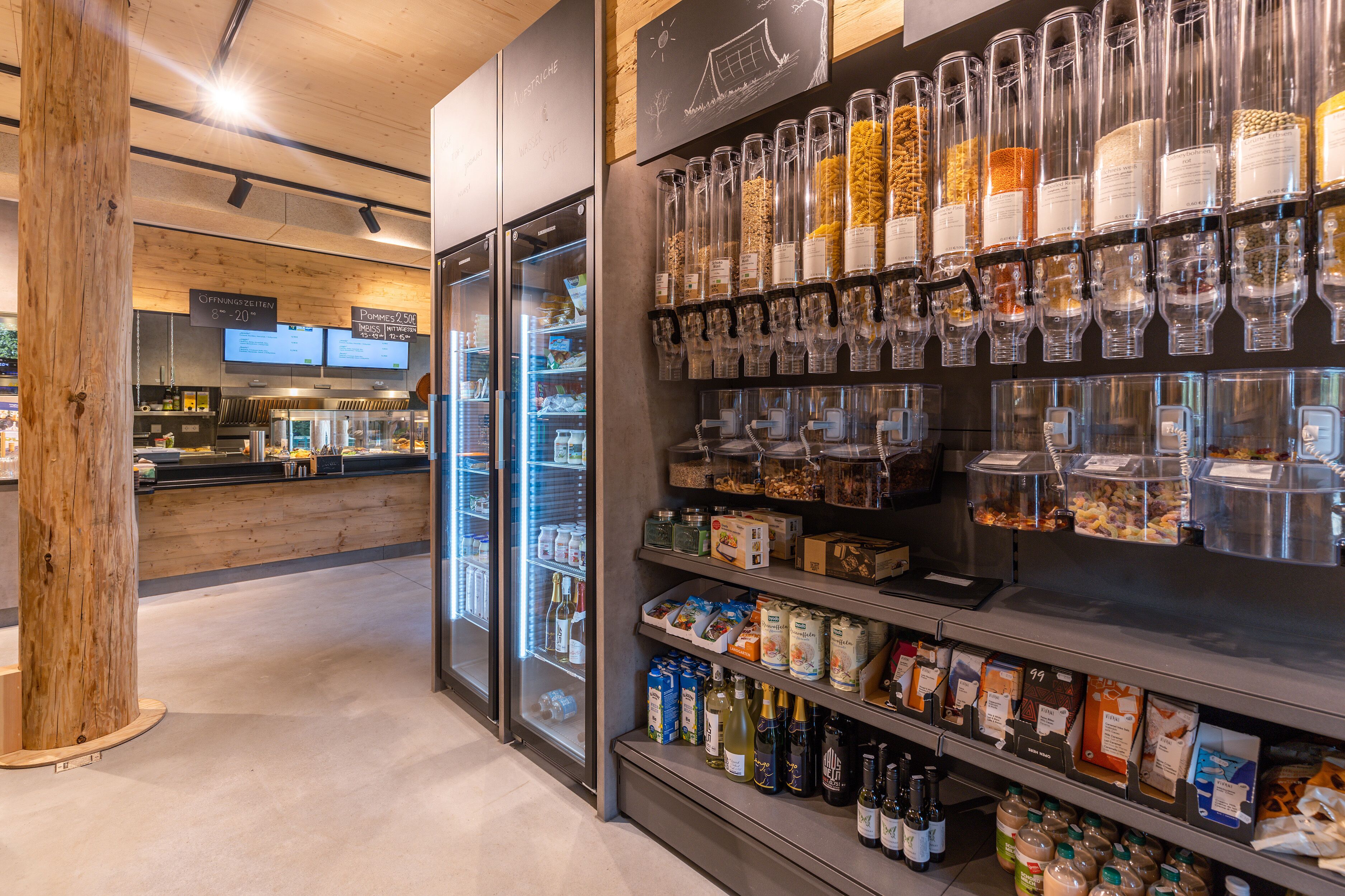 A grocery store interior with refrigerated sections, shelves stocked with beverages, and a wooden pillar.