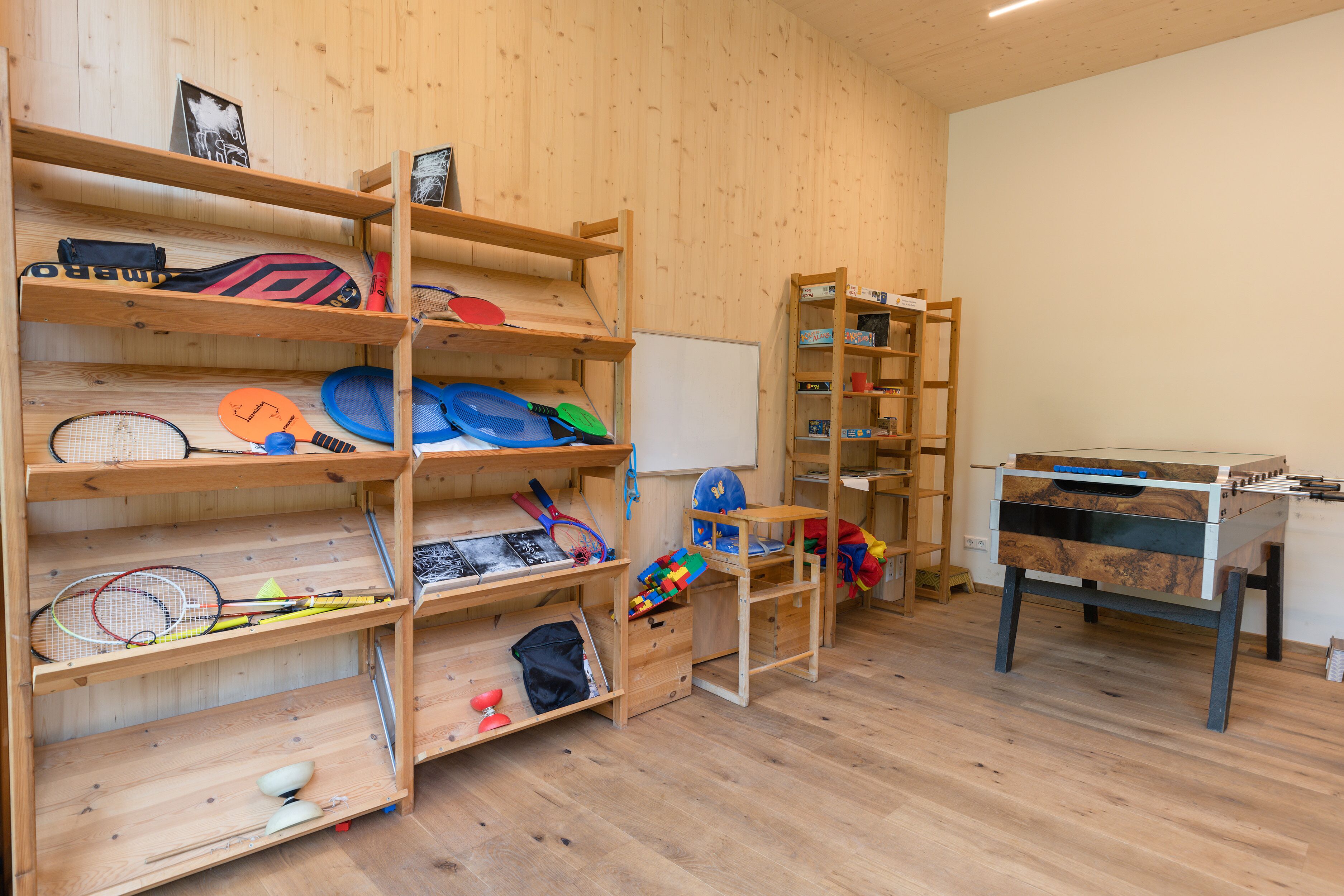 Una habitación con estanterías de madera que contiene equipo deportivo, una pizarra y una mesa de fútbol de mesa.