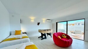 Une chambre d’hôtel moderne avec deux lits, un fauteuil en forme de sac à haricots rouge, une table de baby-foot et une grande fenêtre donnant sur la ville.