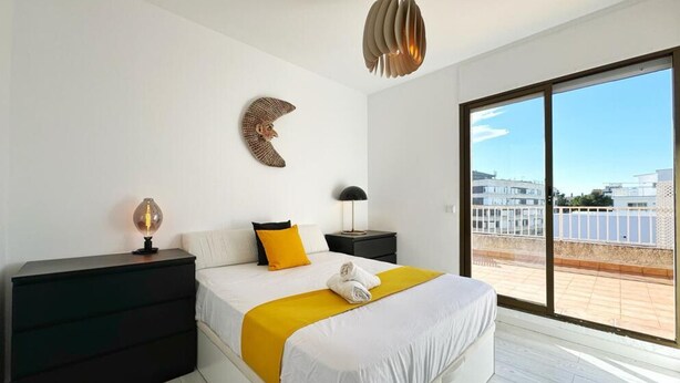 Une chambre d’hôtel moderne dotée d’un grand lit, d’une table de chevet, d’une lampe, d’une œuvre d’art murale et offrant une vue sur la ville grâce à de grandes fenêtres.