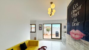 Un salon lumineux avec un canapé jaune, un lustre et une grande affiche accrochée au mur.
