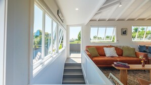 Un amplio salón con una escalera que lleva a un balcón, un sofá naranja confortable y una mesa de centro de madera.