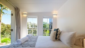 Un dormitorio con cama, cortinas y dos ventanas que dan a zonas verdes.