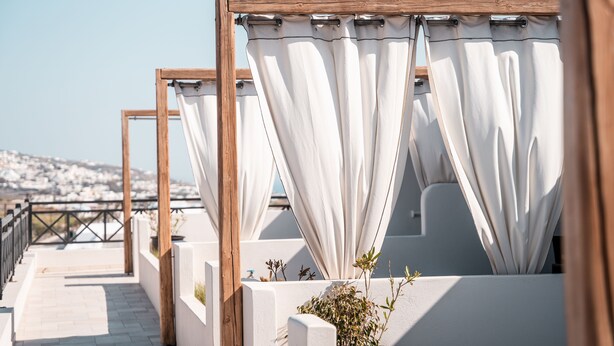 A balcony with white curtains and a wooden frame, overlooking a cityscape. - IfestAu.4 Suites Superior sea view (Santorini)