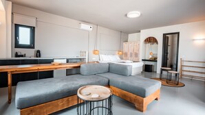 A modern living space with a grey sectional sofa, wooden coffee table, and a small round table with a candle. - IfestAu.4 Suites Superior sea view (Santorini)