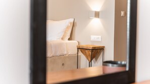 Moderni hotellihuone, jossa on sänky, yöpöytä ja peili, joka heijastaa huonetta.