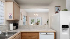 A modern kitchen with wooden cabinets, a dishwasher, a water dispenser, and a view of the backyard through a glass door. - Casa Caracol - Pool - Walk to the Beach, WiFi (South Padre Island)