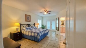 A bedroom with a bed, bedside tables, a ceiling fan, a door leading to a bathroom, and a window. - Casa Caracol - Pool - Walk to the Beach, WiFi (South Padre Island)