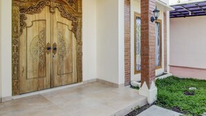 A large wooden door with intricate carvings, a brick column, and a small garden area with grass and a pathway. - Capital O 93718 Homestay 3 Bidadari (Moyudan)