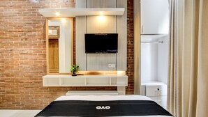 A modern hotel room with a brick wall, a mounted TV, a white vanity with a mirror, and a bed with a black and white bedspread. - Capital O 93718 Homestay 3 Bidadari (Moyudan)