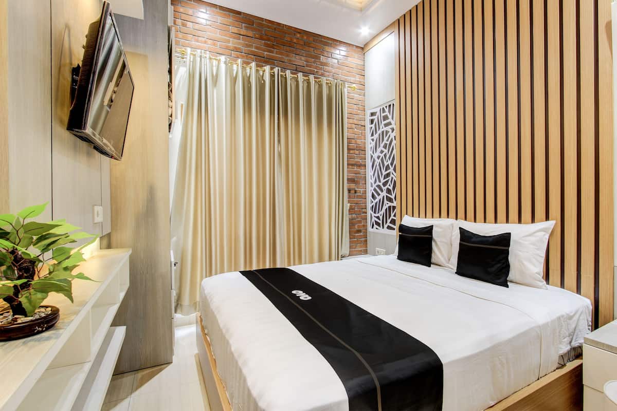 A modern hotel room with a large bed, a TV mounted on the wall, a potted plant, and a curtain with a geometric pattern.