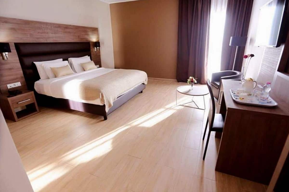 A modern hotel room with a large bed, bedside tables, a small desk, and a chair.
