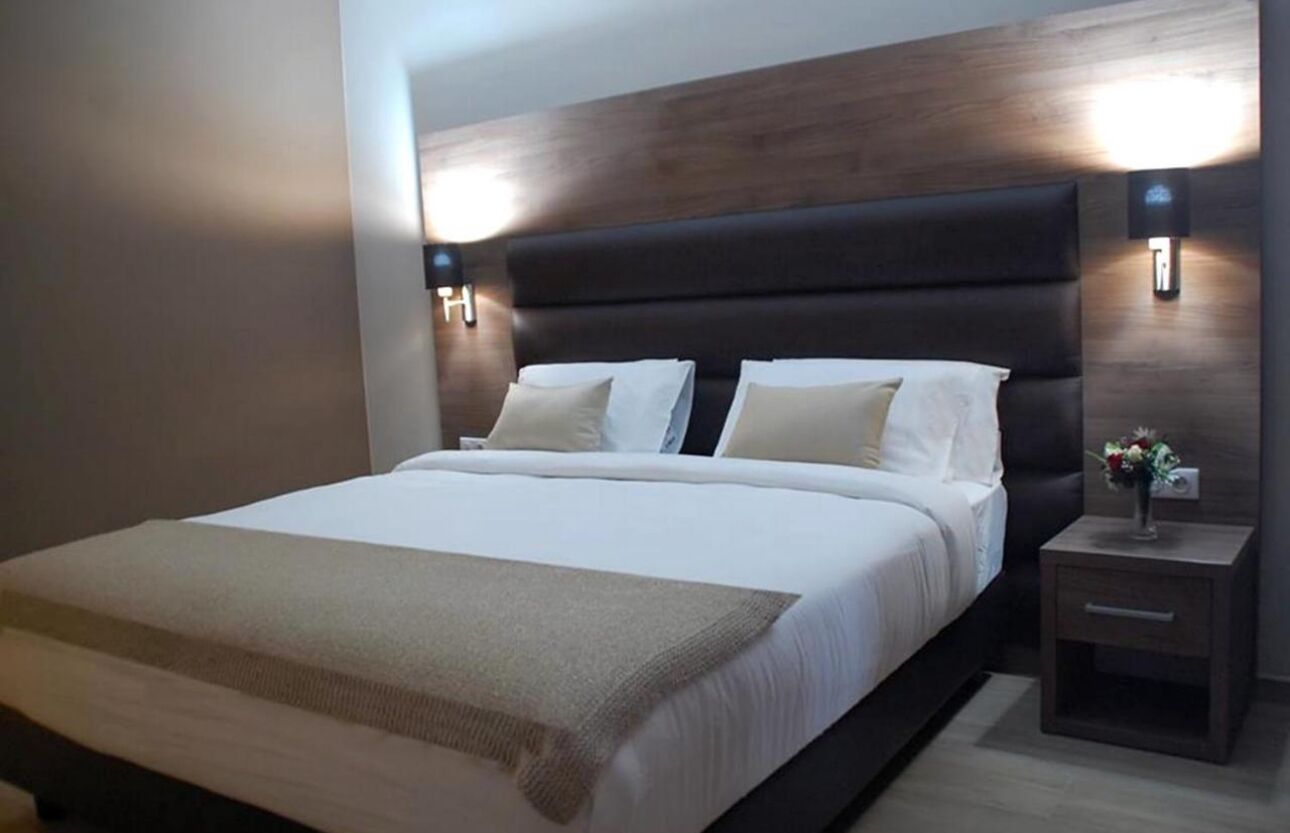 Une chambre moderne avec un grand lit, deux tables de chevet et des lampes fixées au mur.