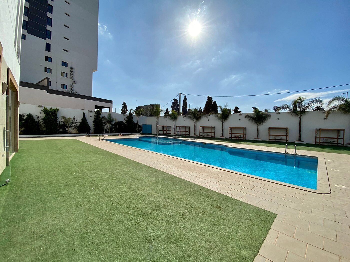 A swimming pool with a clear blue water, surrounded by a paved area and a grassy lawn.