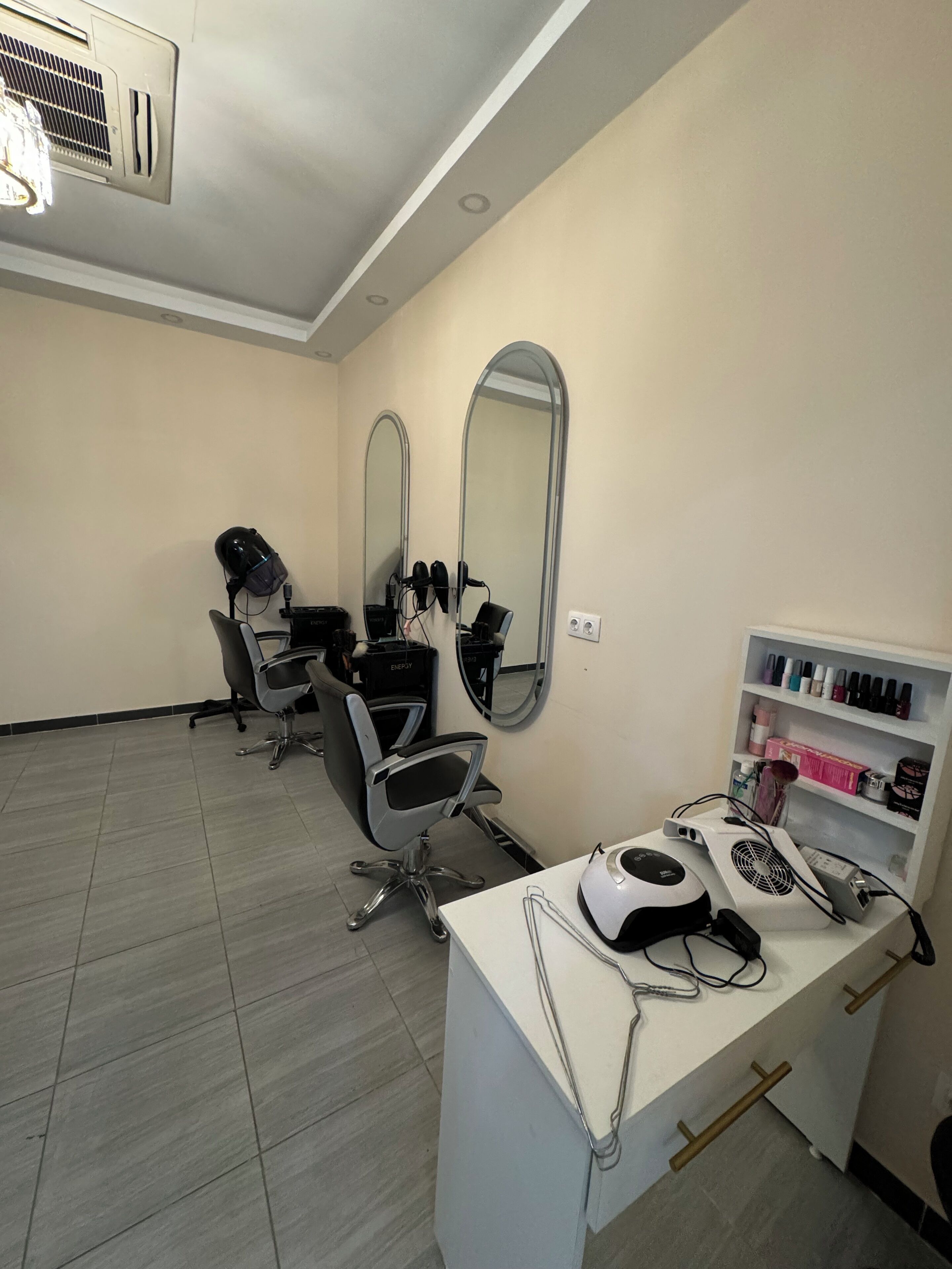 A salon with a white desk, two chairs, mirrors, and shelves with hair products.