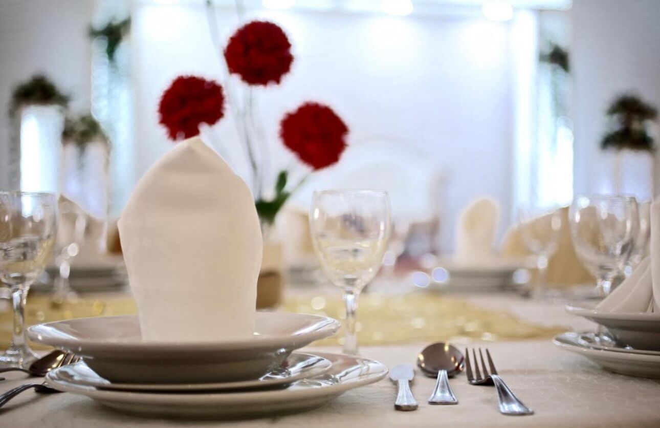 A table set for a meal with white plates, silverware, and wine glasses.