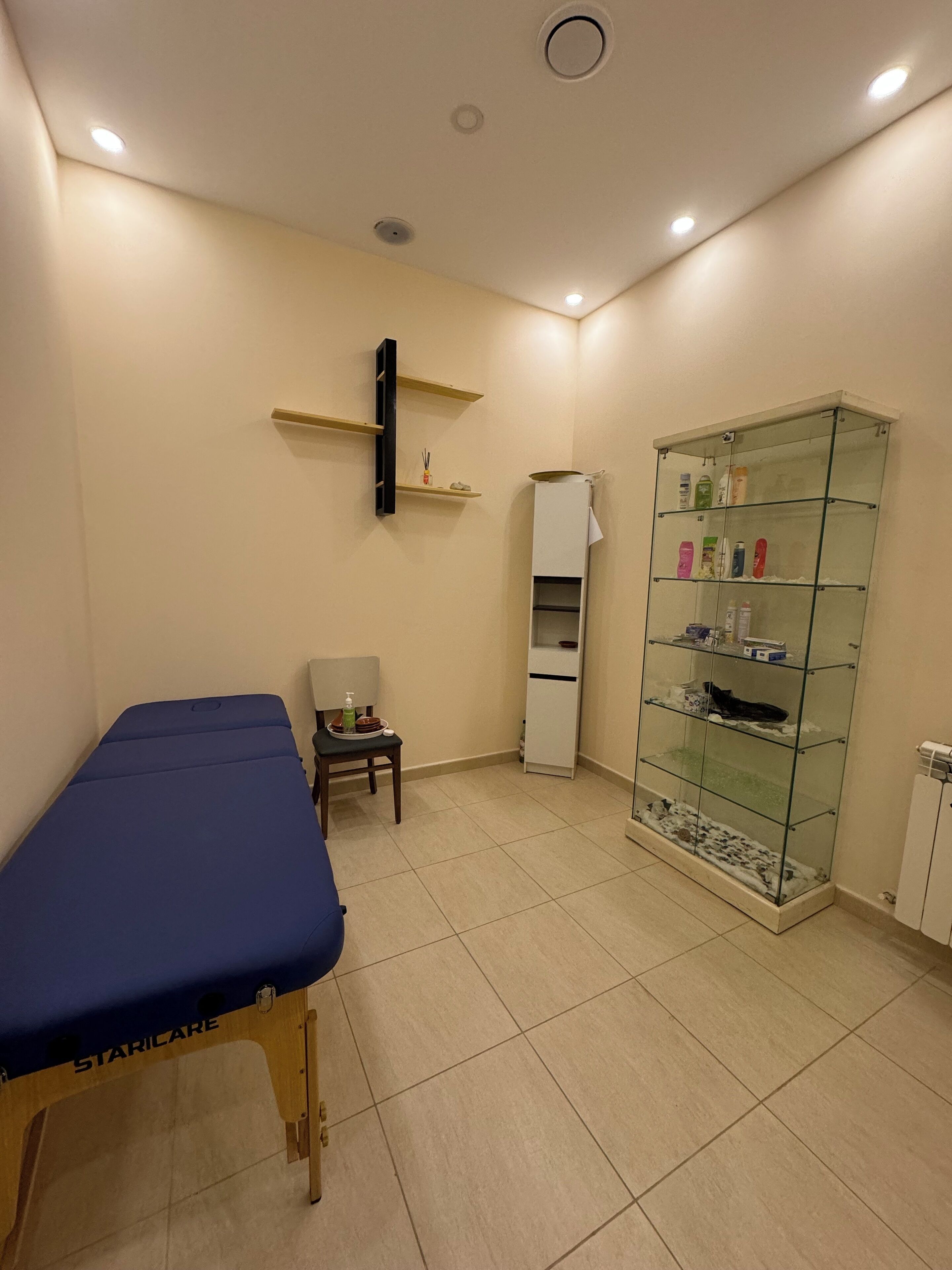 Une salle d’examen clinique équipée d’un lit médical, d’une chaise, d’une armoire en verre contenant du matériel médical et d’une armoire blanche.