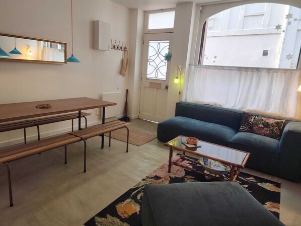 Un salon comprenant un canapé, une table basse, une table à manger avec des bancs, un miroir et une fenêtre donnant sur un paysage.