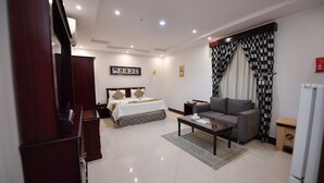 Una habitación de hotel moderna con cama, sofá, mesa de centro y una mesita con lámpara.
