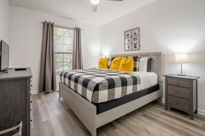 A bedroom with a bed, a bedside table, a lamp, a TV, and a window with curtains.