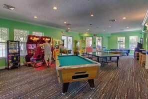 A pool table, arcade machines, and a billiards table in a room with patterned carpet and green walls.