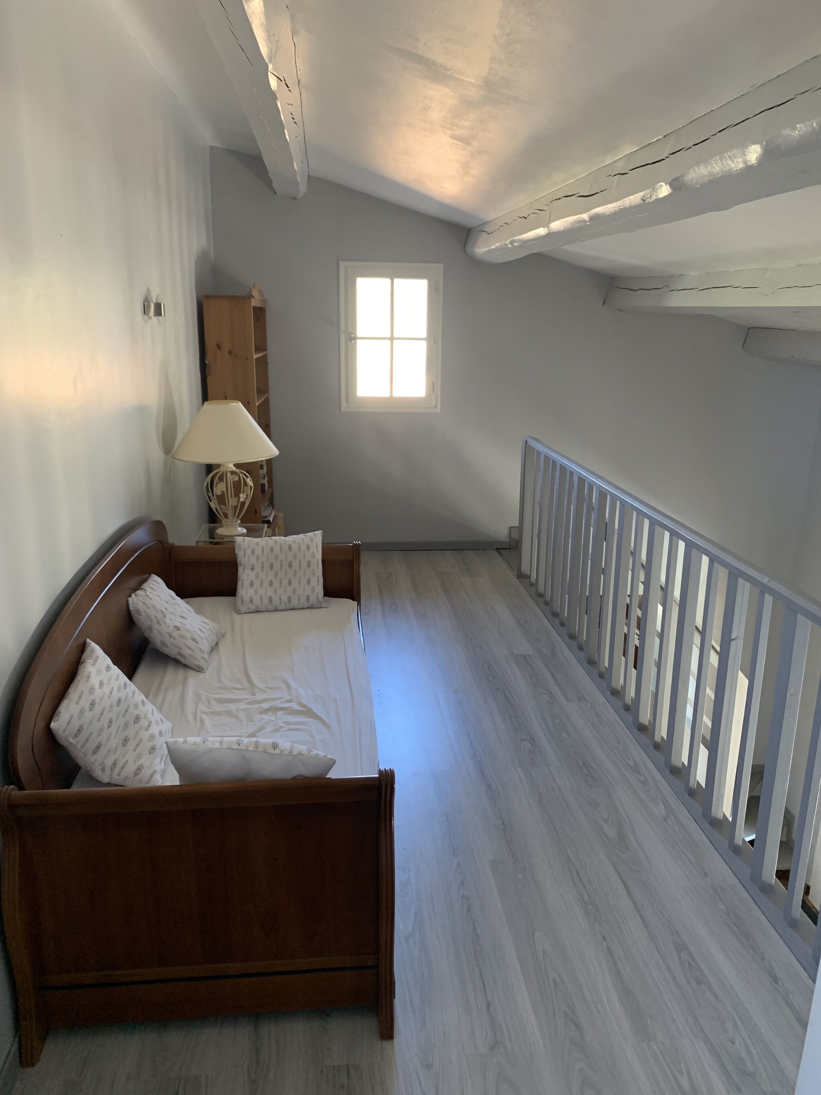 Een slaapkamer met een houten bed, een nachtkastje, een lamp en een raam.