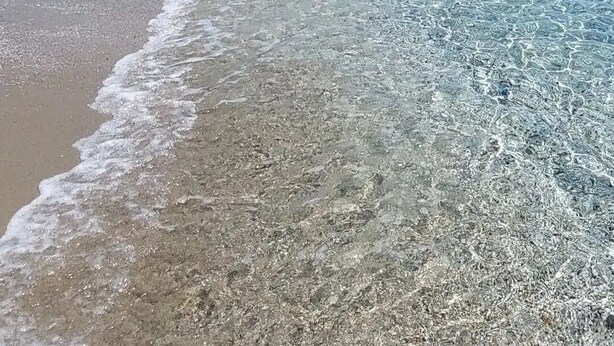 Een strand met helder ondiep water, een zandstrand en bergketens in de verte.