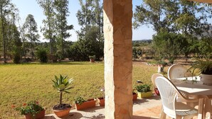 Een terras met een tafel en stoelen, omringd door plantenpotten en uitzicht op een grasveld met bomen.