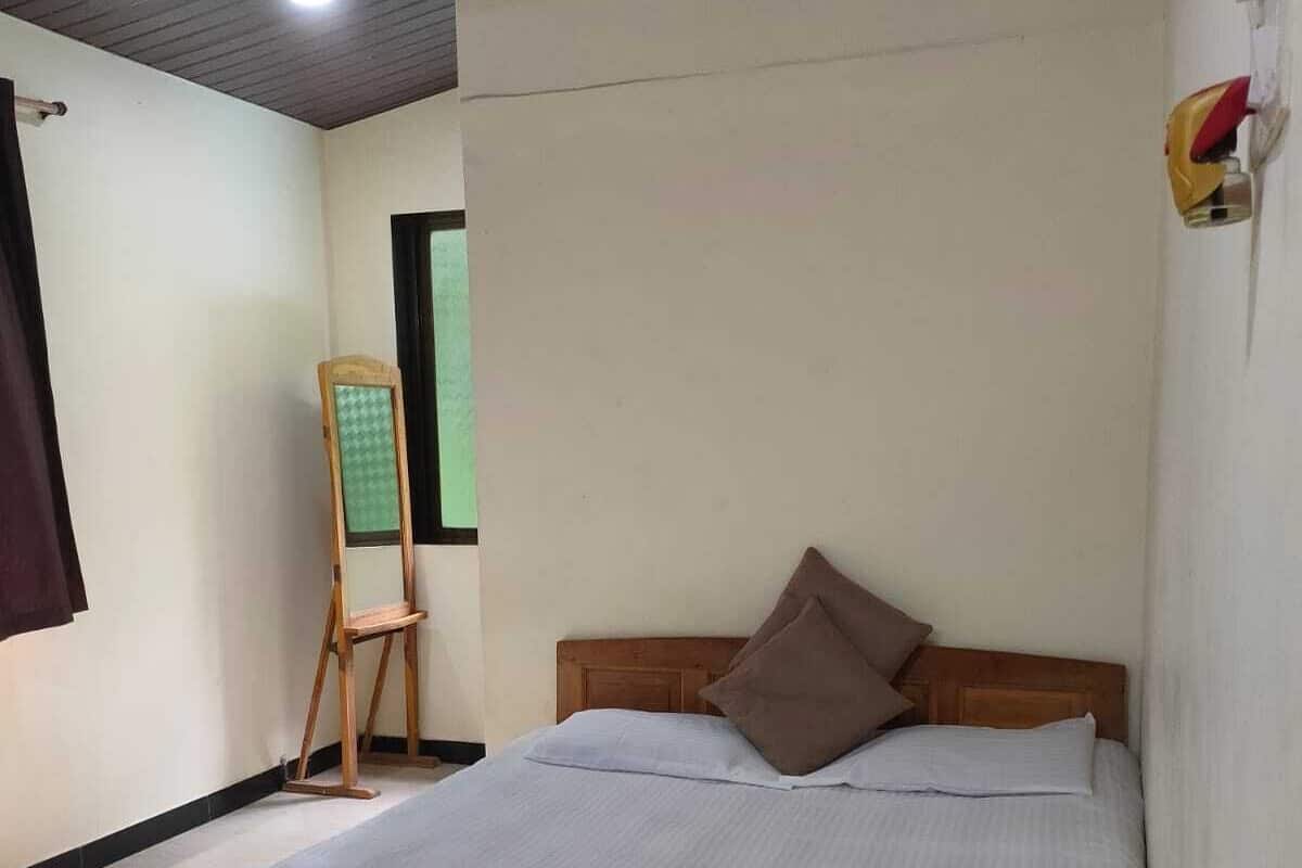 A neatly made bed with a wooden frame and white bedding in a room with a wooden ceiling and a small standing mirror.