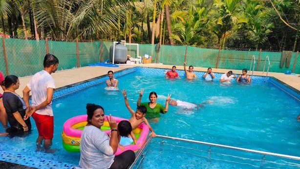 Una piscina con gente disfrutando del agua, rodeada por una valla y palmeras.