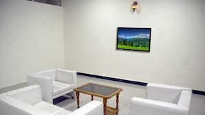 Una habitación con muebles blancos, una mesa con cubierta de vidrio y una pintura de paisaje enmarcada en la pared.