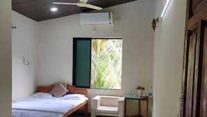 Un dormitorio con cama, una silla, un escritorio, un ventilador de techo y una ventana con vistas a palmeras.