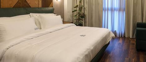 A neatly made bed with white linens, a green upholstered headboard, and a wooden wall panel design.