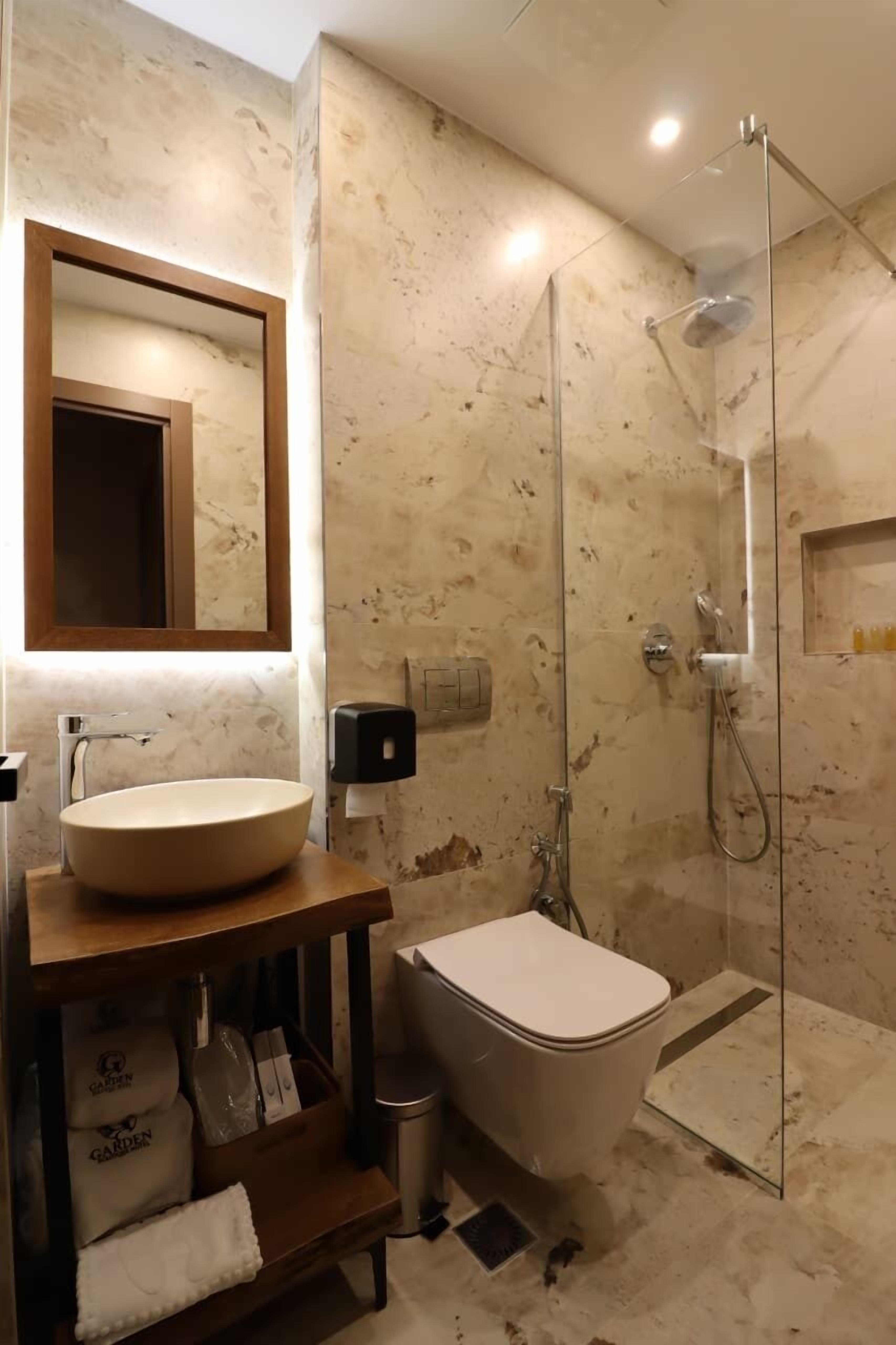 Ein Badezimmer mit einer freistehenden Badewanne, einer gläsernen Duschkabine, einer marmorierten Wand und einem Holzwaschtisch mit Waschbecken und Handtuchhalter.
