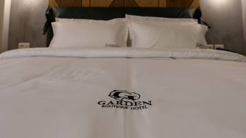 A neatly made bed with a white bedspread featuring the logo and name of the Garden Boutique Hotel.