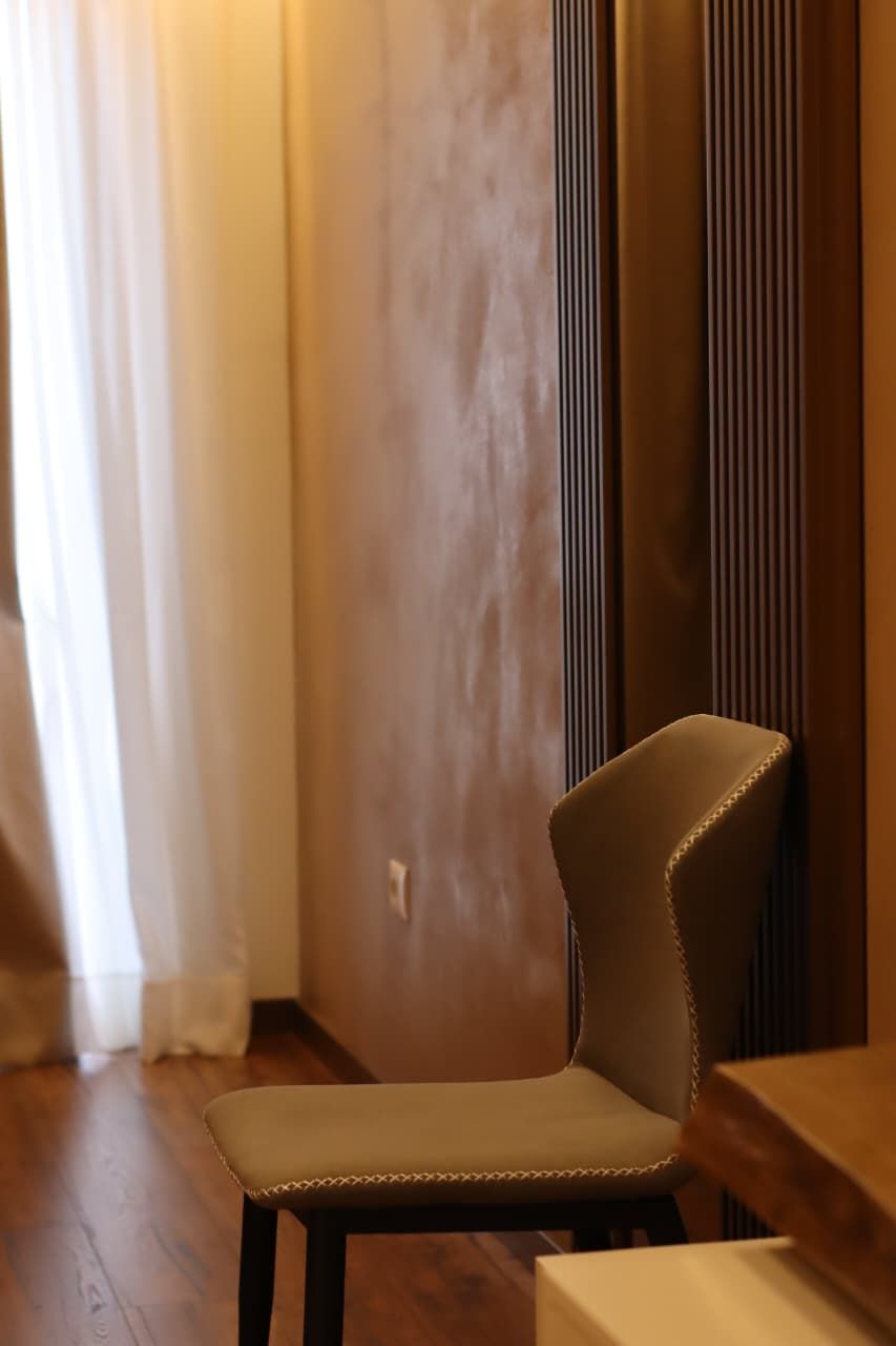 A chair in a corner of a room with a wooden floor and a textured wall.