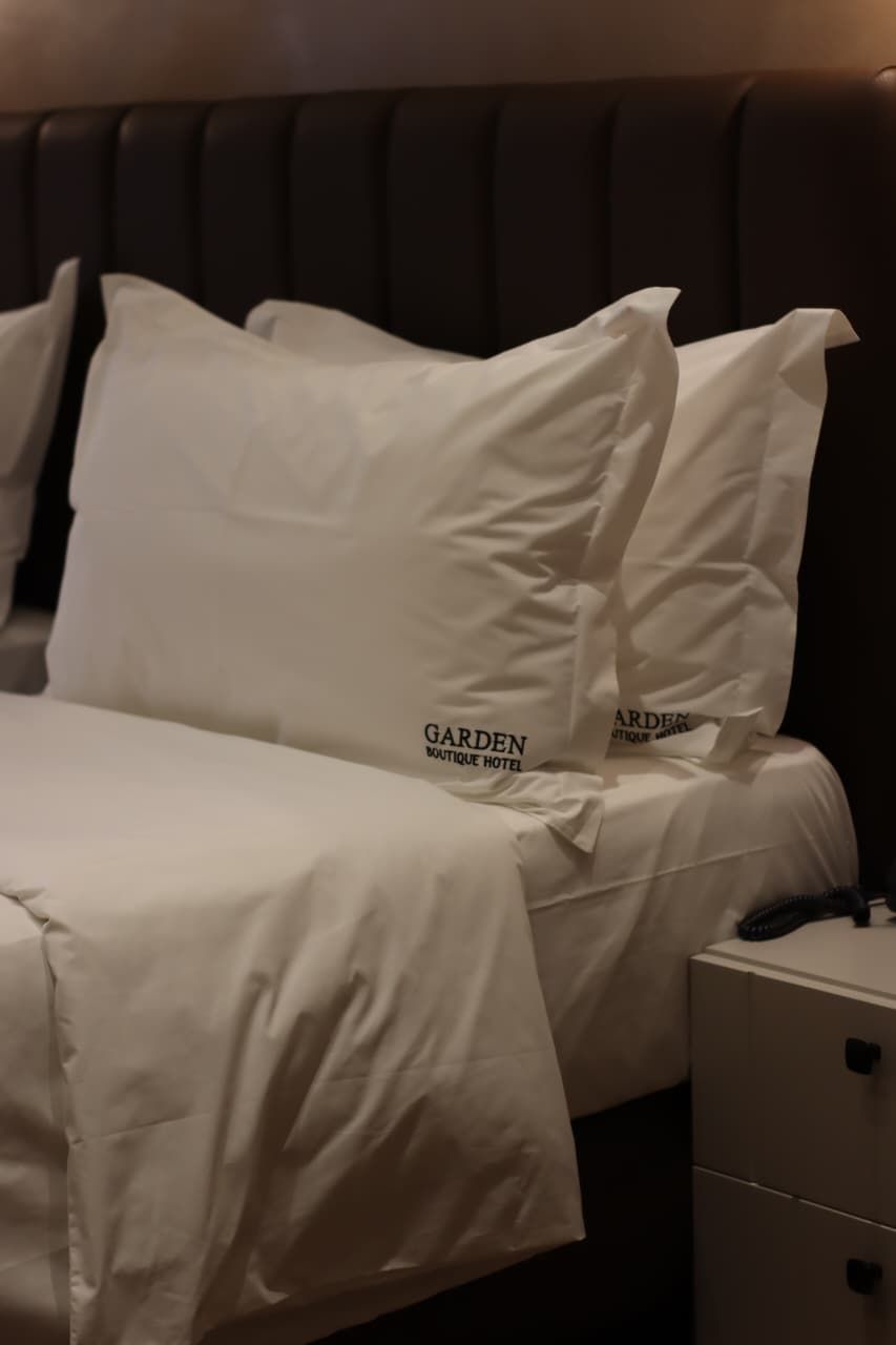 A neatly made bed with white bedding and pillows, a bedside table with a telephone, and a headboard.