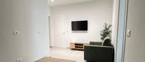 Uma sala de estar moderna com uma mesa de centro de madeira, um sofá cinzento e uma TV de tela plana na parede.