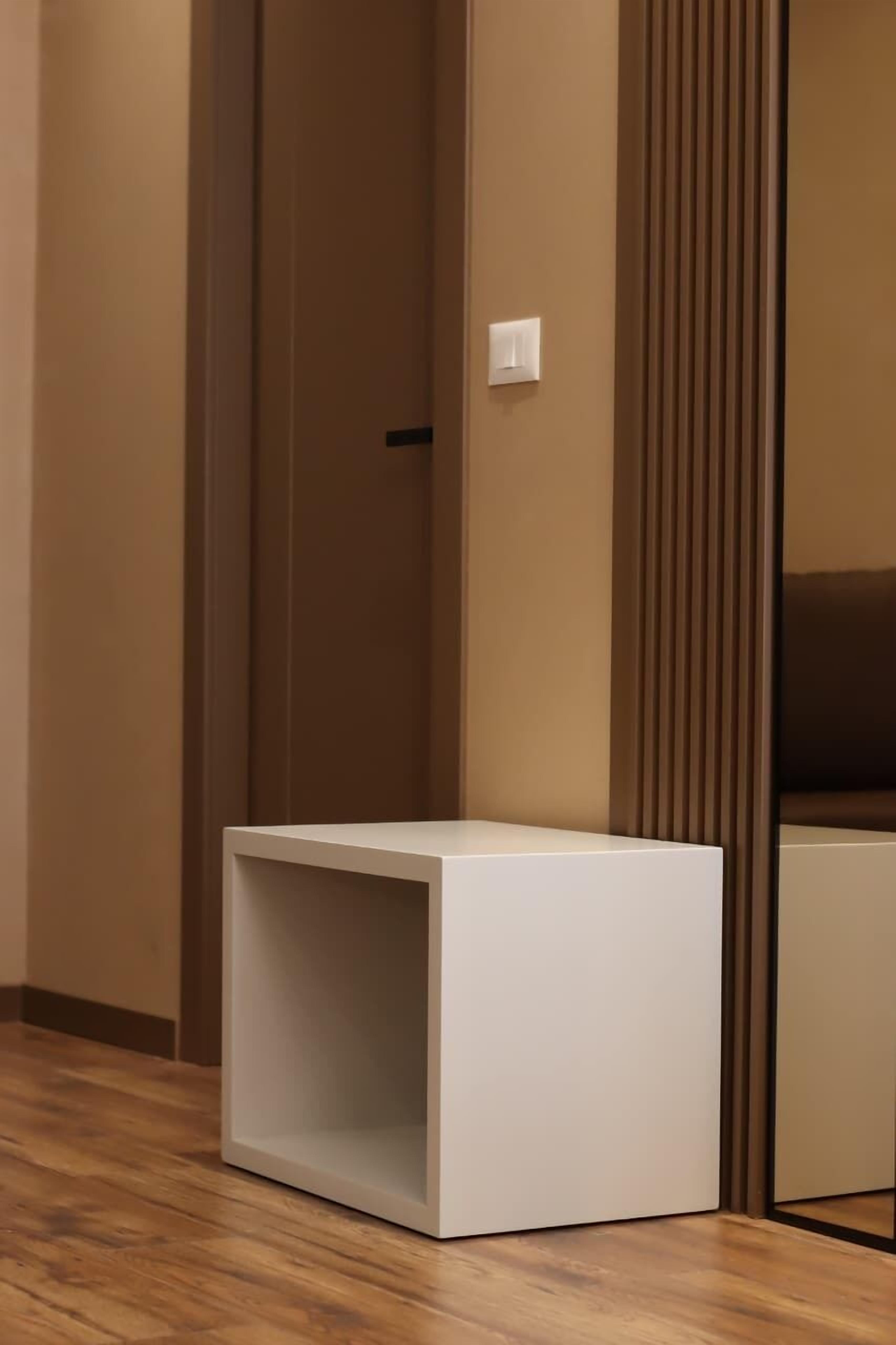 Una habitación con piso de madera, una mesita auxiliar blanca, una puerta y una pared con líneas verticales.