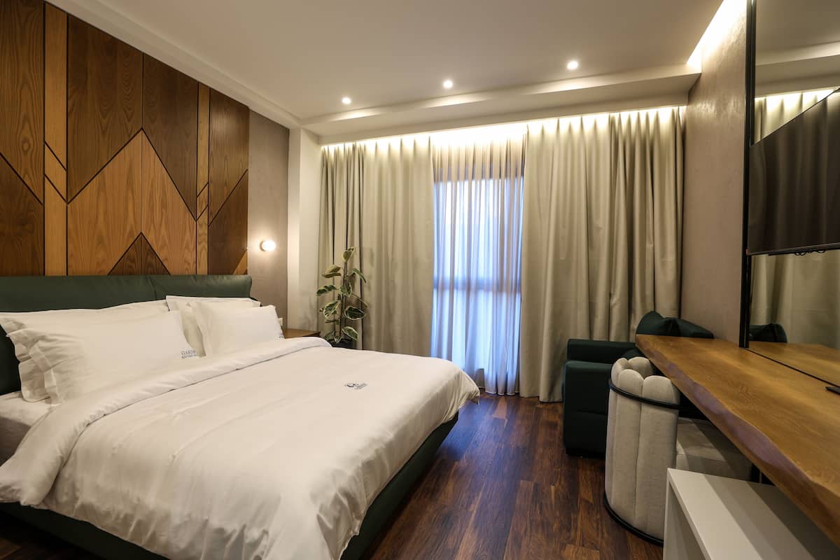 Een moderne hotelkamer met een groot bed, een houten accentmuur, een bureau en een groot raam met gordijnen.