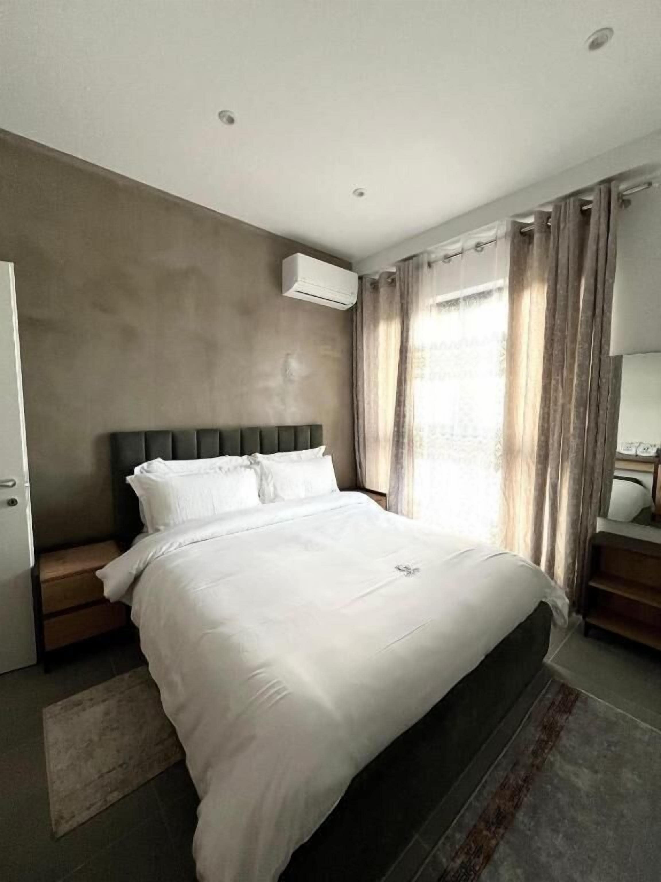 A modern bedroom with a large bed, a built-in headboard, an air conditioning unit, a bedside table, and a nightstand.