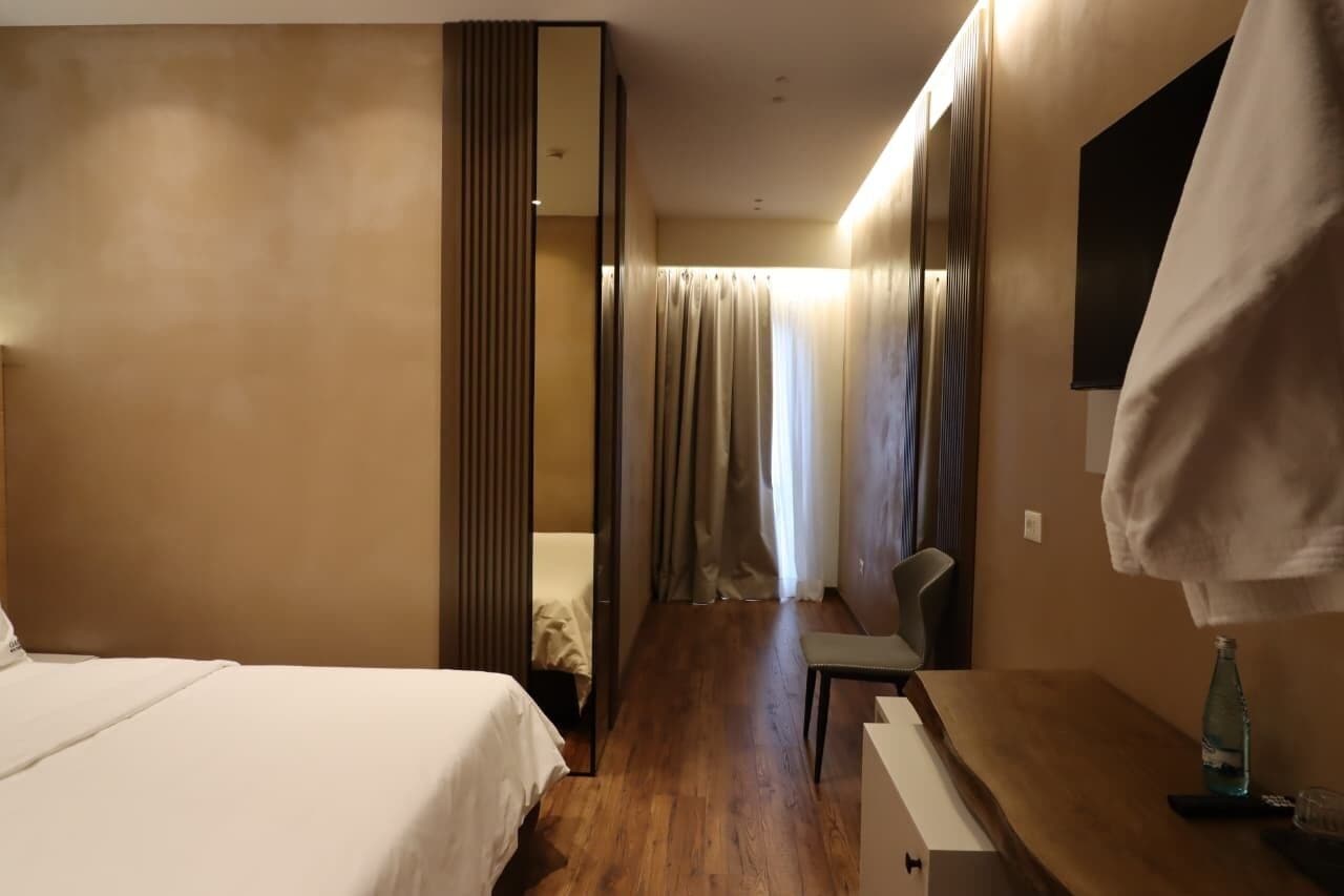 Ein Hotelzimmer mit Bett, Schreibtisch, Stuhl, Spiegel und einem fensterbepflanzten Fenster.
